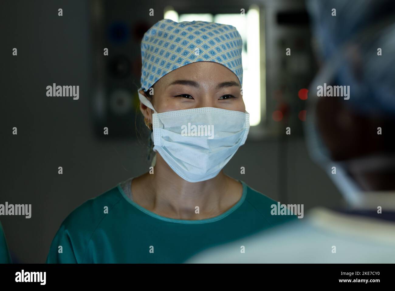 Asiatische Chirurg-Frau, die während der Operation eine Kollegin im Operationssaal anlächelt Stockfoto