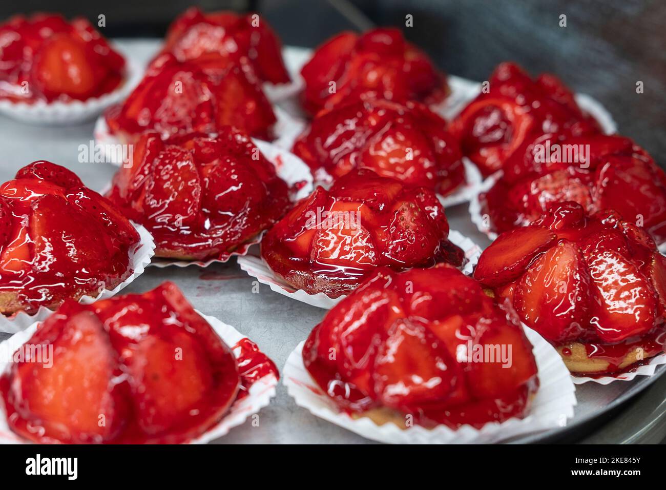Großes Tablett mit köstlichen Erdbeertörtchen, Minitörtchen gefüllt mit süßem Pudding und gekrönt mit Scheiben saftiger roter Beeren, Gelifiziertem Sirup Stockfoto