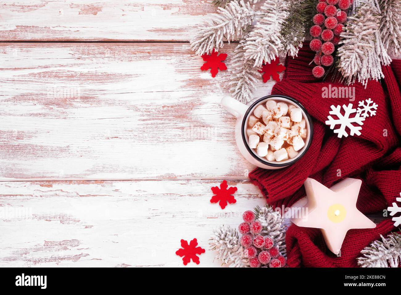 Gemütlicher Weihnachts- oder Winterrand mit rotem Pullover, Kerze, heißer Schokolade, frostigen Ästen und Dekor. Blick von oben auf eine rustikale, weiße Holzunterseite Stockfoto