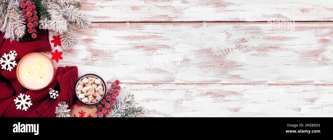 Gemütliche Weihnachts- oder Winterecke mit rotem Pullover, Kerzen, heißer Schokolade, frostigen Ästen und Dekor. Blick über ein rustikales weißes Holzbanner Stockfoto