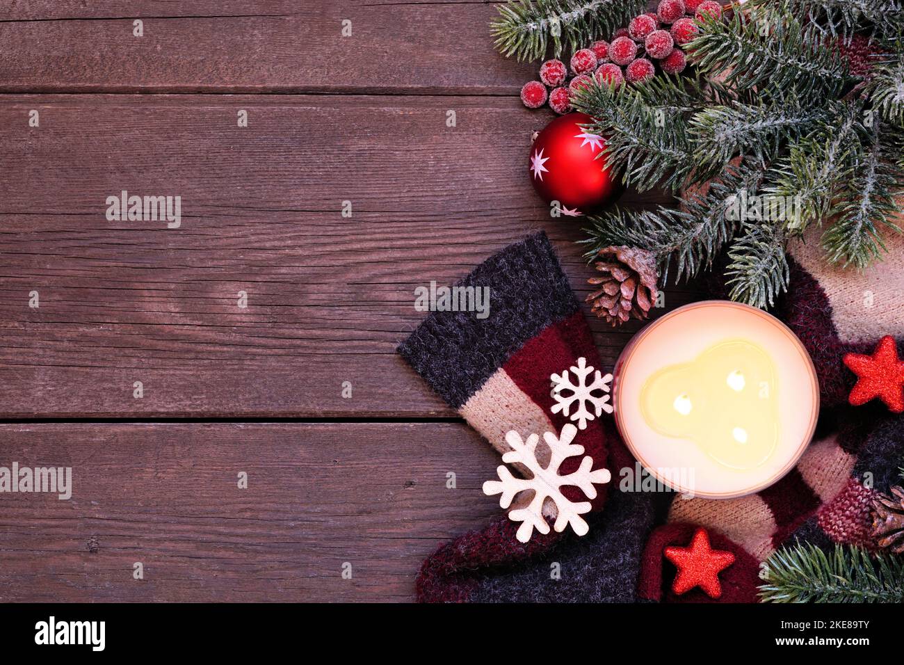 Gemütlicher Weihnachts- oder Winterrand mit rotem, schwarzem und beigefarbenem Pullover, Kerze, Ästen und Dekor. Blick über einen dunklen Holzhintergrund. Stockfoto