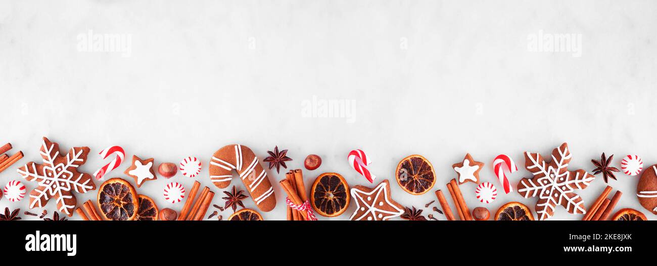 Weihnachtliche Backbordüre mit Keksen, Pfefferminzen und Gewürzen. Draufsicht über einen weißen Marmorhintergrund mit Kopierraum. Feiertagsbackkonzept. Stockfoto