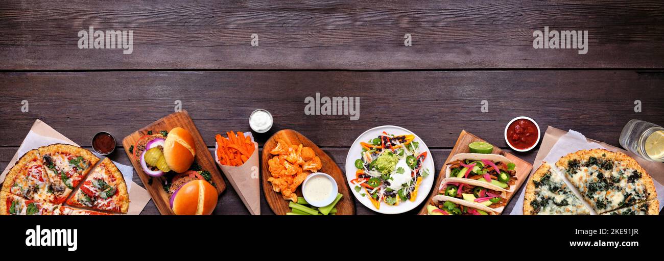 Gesunde pflanzliche Fast-Food-Grundgrenze. Draufsicht über einen dunklen Holzbanner Hintergrund. Tischszene mit Blumenkohlkruste Pizzas, Bohnenburgern, Mus Stockfoto