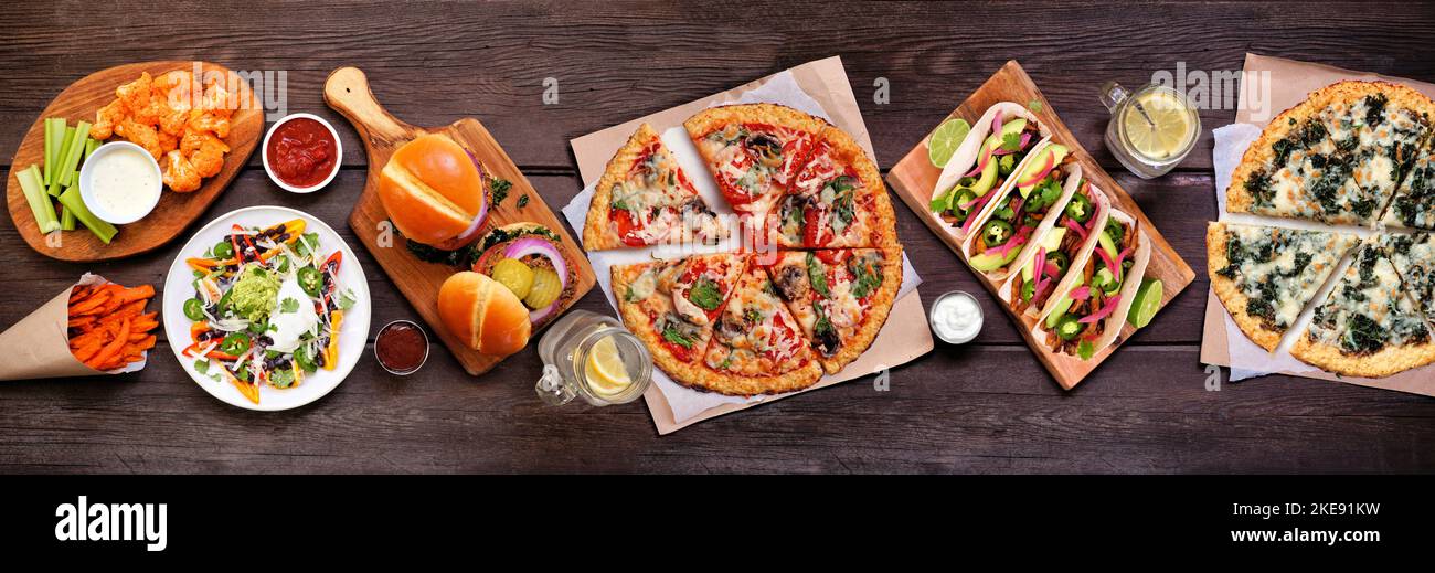Gesunde Pflanze basiert Fast-Food-Tabelle Szene. Oben auf einem Holzbanner Hintergrund. Pizzas aus Blumenkohlkruste, Bohnenburger, Pilztacos und Vegetari Stockfoto