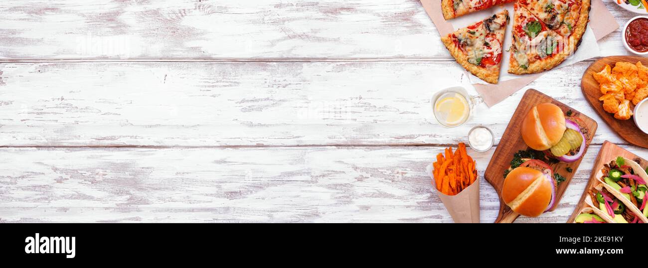 Gesunde pflanzliche Fast-Food-Seitengrenze. Draufsicht über einen weißen Holzbanner Hintergrund. Tischszene mit Blumenkohlkruste Pizza, Bohnenburgern, Stockfoto