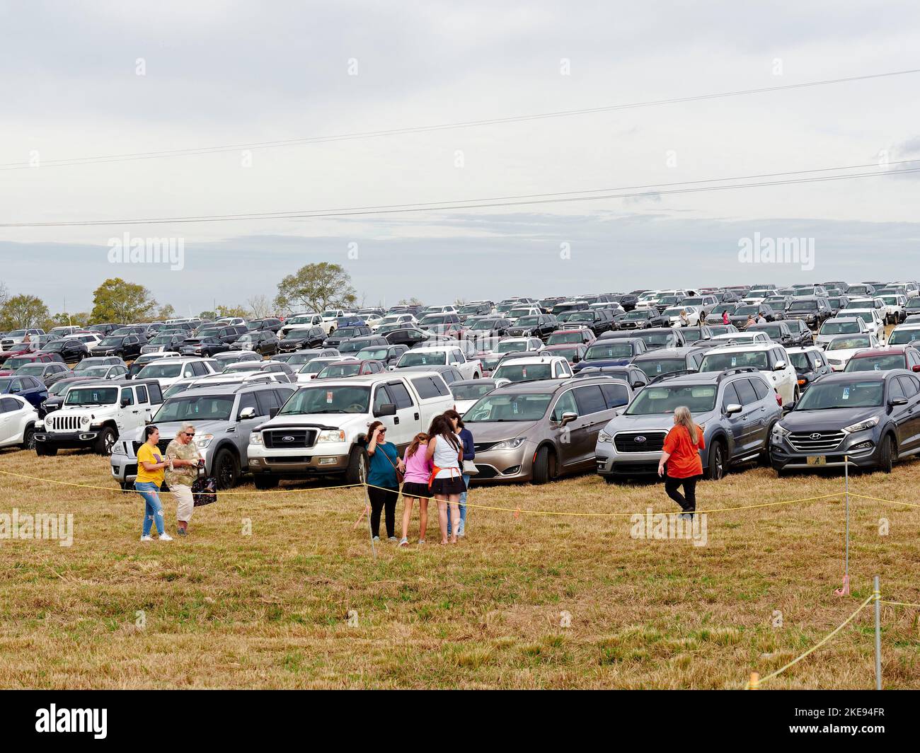Menschen, die auf einem Grasfeld auf einer lokalen Kunsthandwerksmesse in der Pike Road Alabama, USA, aus Reihen geparkter Autos und SUV-Fahrzeuge laufen. Stockfoto