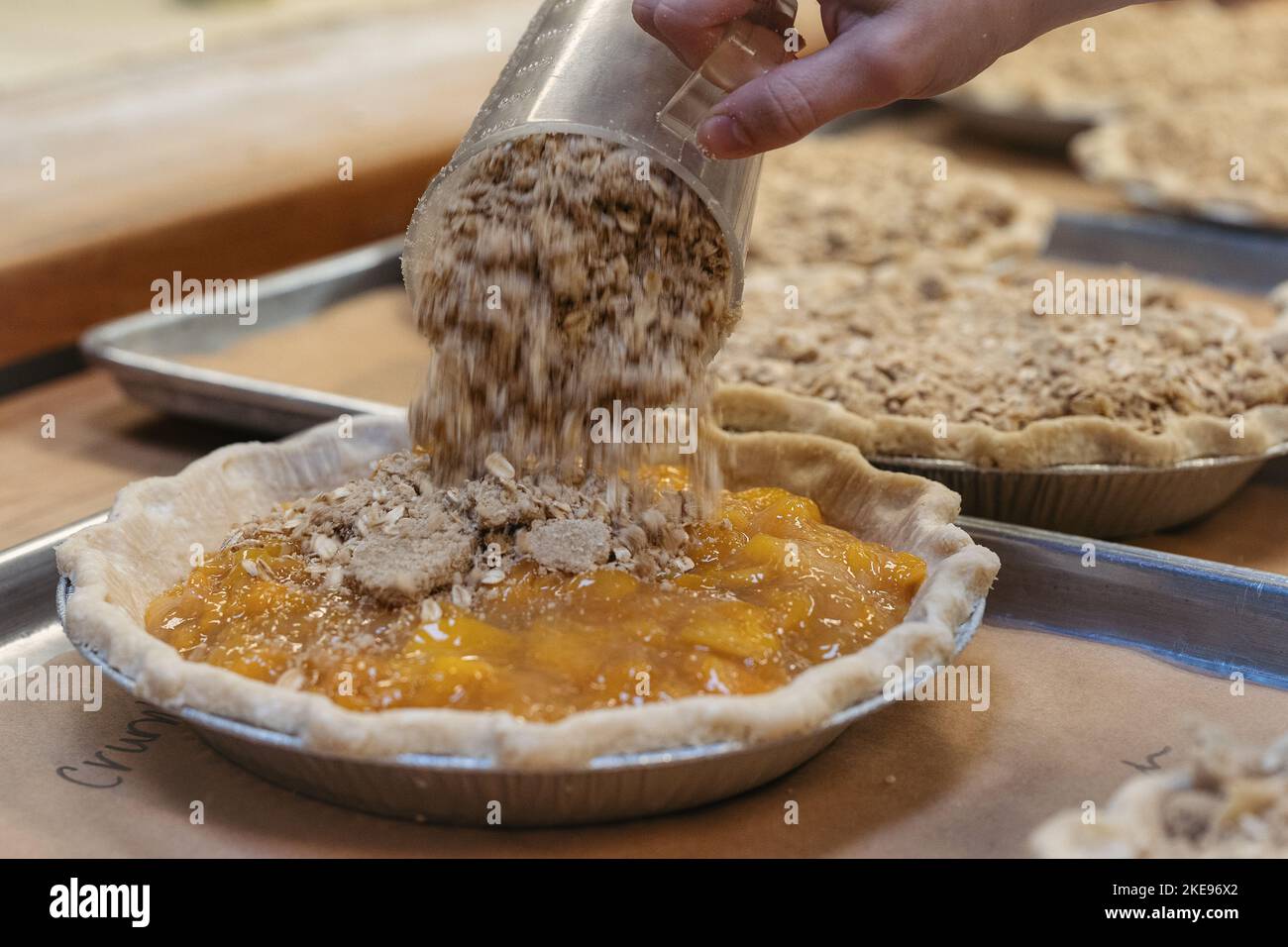 Ein glutenfreier Belag wird auf einen Kuchen mit Pfirsichfüllung gegossen Stockfoto