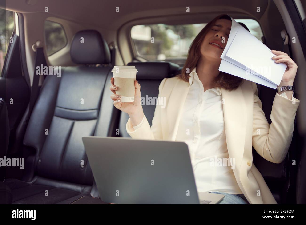 Eine junge Frau bedeckt ihr Gesicht mit einem Papierkram, während sie arbeitet und schlechte Nachrichten über ihren Job in ihrem Auto aufgibt. Stockfoto