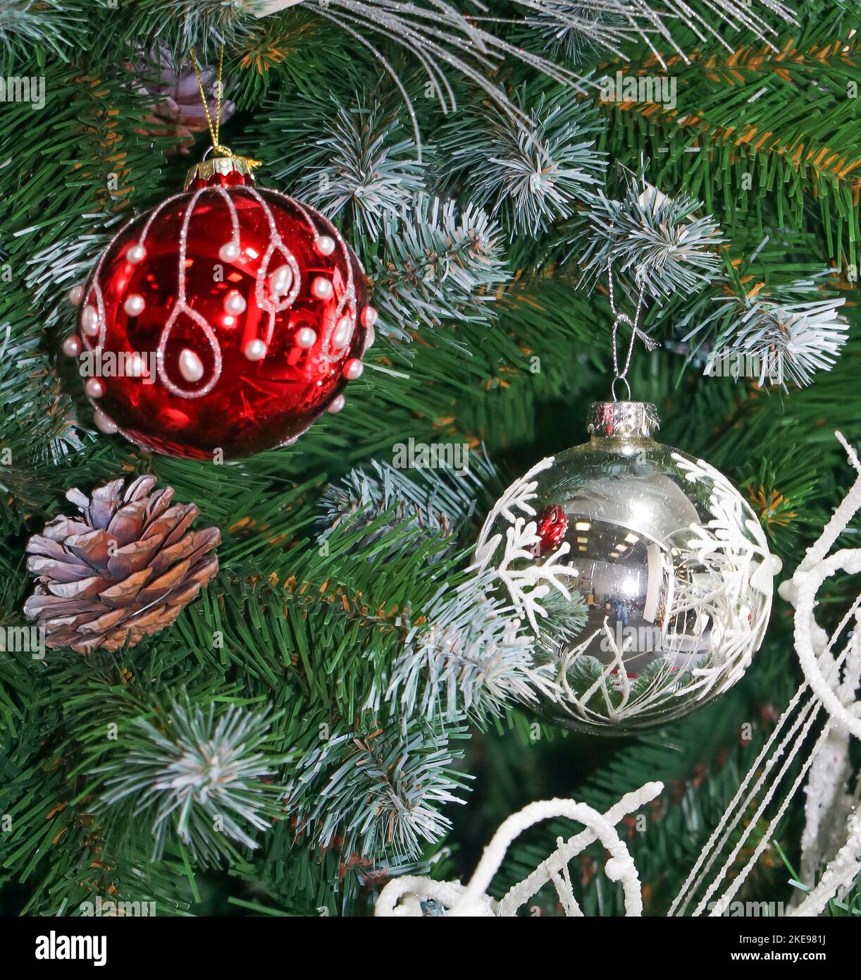 Große Weihnachtsbaumschmuck, die an einem mit Schnee bedeckten Zweig hängen Stockfoto
