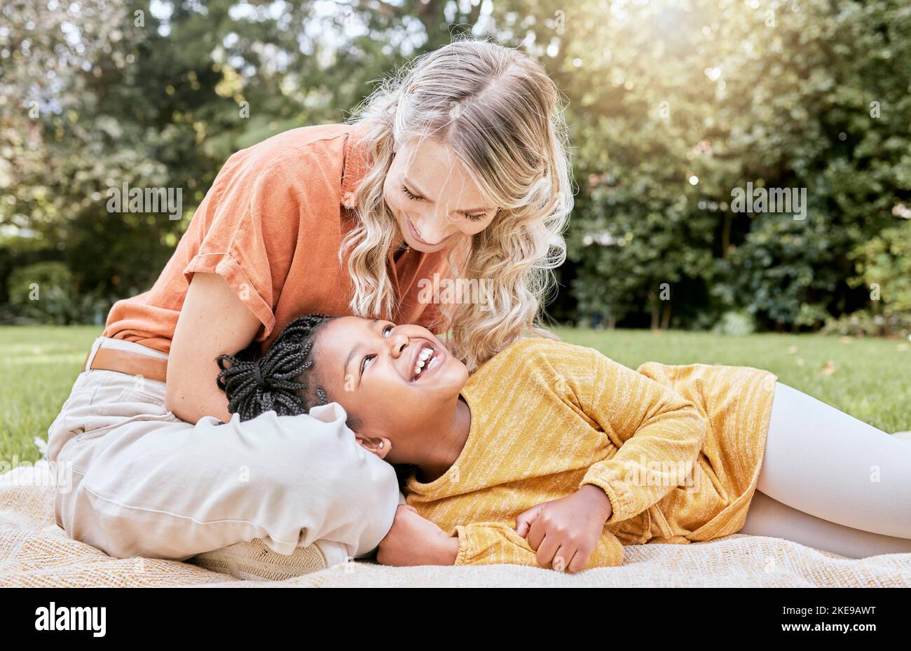 Glückliche Familie, interracial und Mädchen und Mutter entspannen sich in einem Park, glücklich und lächeln, während sie sich auf Gras ausruhen. Liebe, Familie und schwarzes Kind lachen Stockfoto
