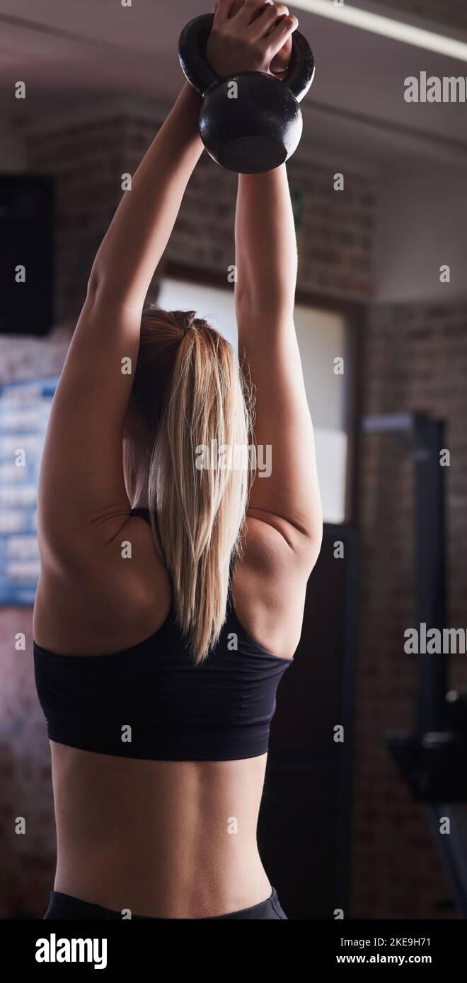 Dampf ablassen nach einem stressigen Tag. Rückansicht einer jungen Frau, die im Fitnessstudio Gewichtheben macht. Stockfoto
