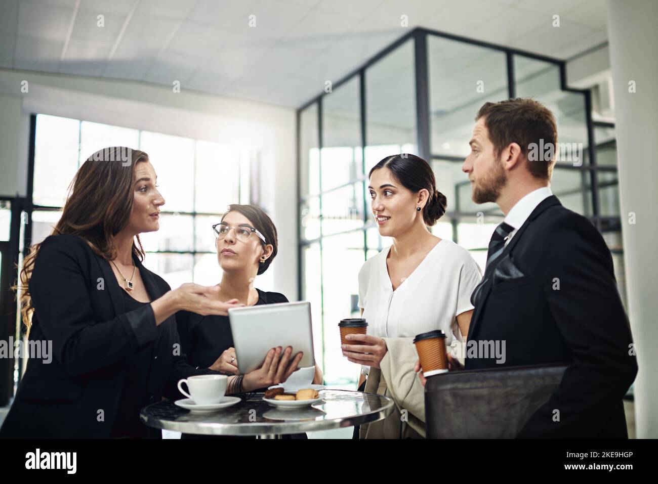 Sehen Sie selbst: Eine Gruppe von Geschäftsleuten, die sich im Büro ein Tablet ansehen. Stockfoto