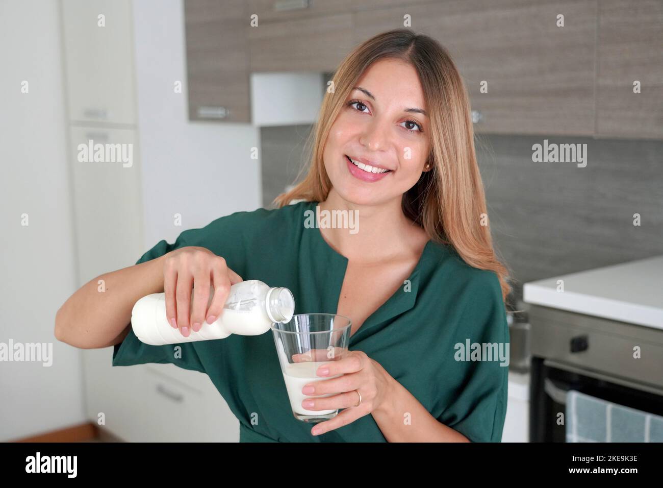 Morning Portrait der jungen lächelnden Frau füllt das Glas mit Kefir. Schönes Mädchen, das Milch trinkt. Schaut auf die Kamera. Stockfoto