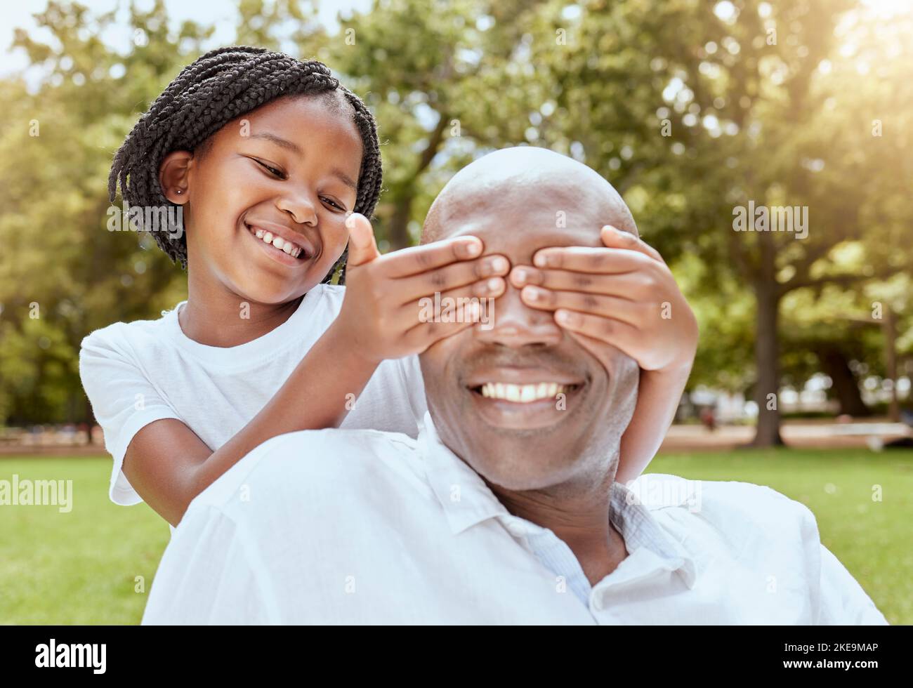 Park, Überraschung und Mädchen mit glücklichen Vater, Hände über die Augen und spielen beim Picknick im Garten. Natur, Liebe und Familie, kleines Kind und schwarzer Mann auf Gras Stockfoto