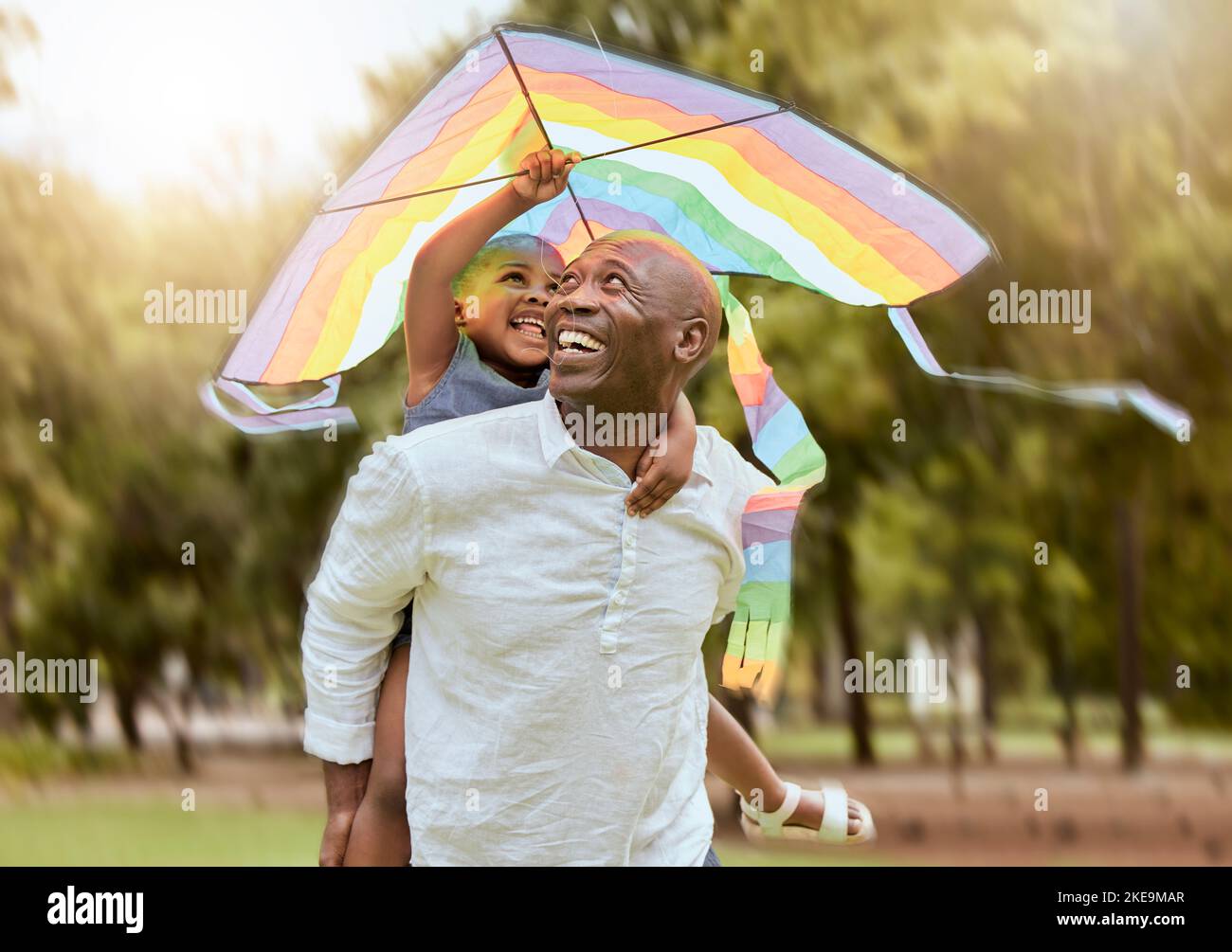 Vater, Kind und Regenbogendrachen im Freien in einem Naturpark für Spaß, Bindung und Vertrauen der Lebensversicherung und Ersparnisse einer schwarzen Familie Spaß haben. Schwarz Stockfoto