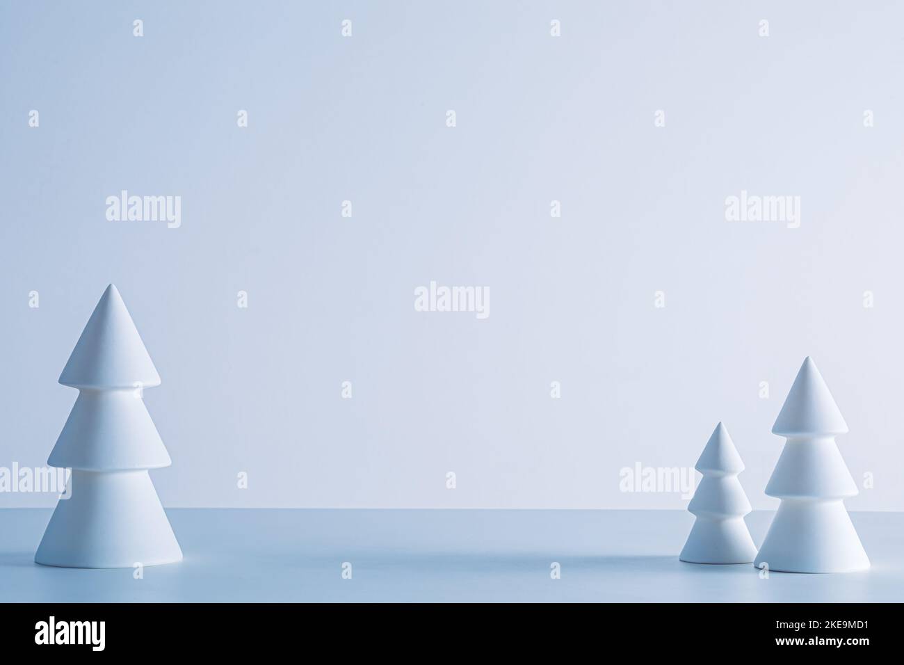 Kleine keramische Weihnachtsbäume auf weißem Hintergrund in kaltem, weichem Winterlicht Stockfoto