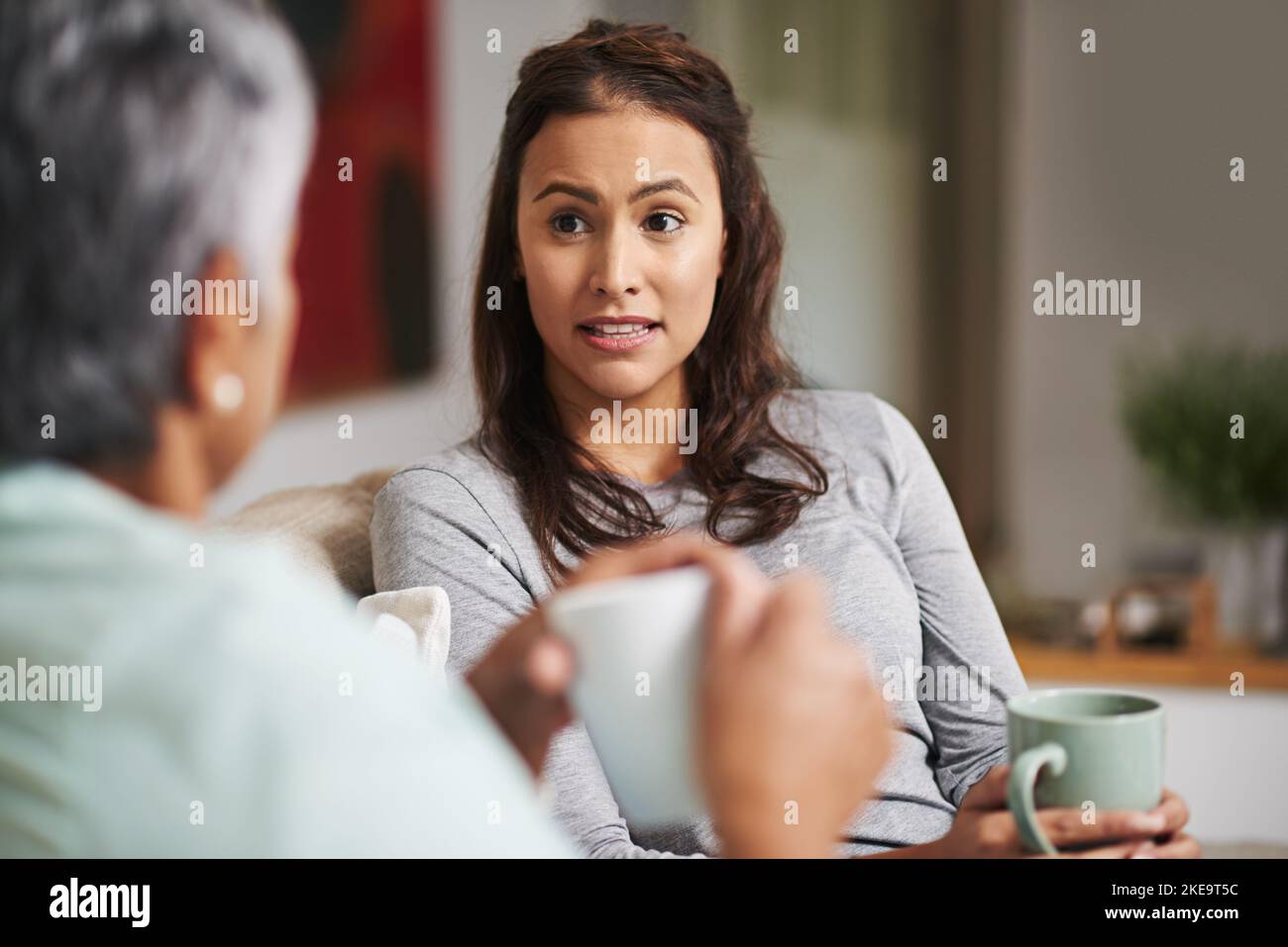 Nein, wirklich. Eine junge Frau und ihre Mutter holen sich auf dem Sofa, während sie Kaffee trinken. Stockfoto