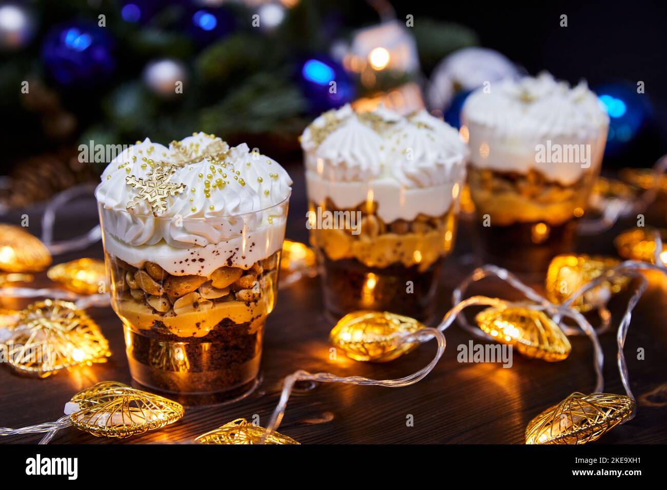 Weihnachts-Kleinigkeiten in Tassen als Dessert, verziert mit Karamell-Schneeflocken, für einen festlichen Tisch auf einem Hintergrund glühender Girlanden Stockfoto