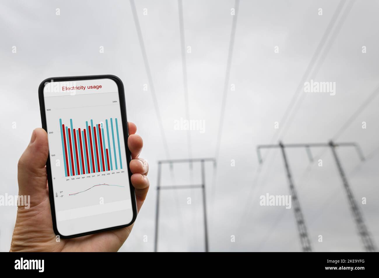 Hand mit Smartphone und Stromleitung im Hintergrund Stockfoto