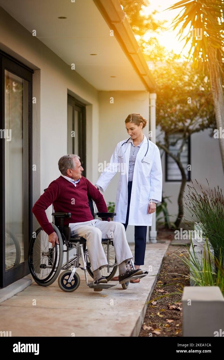 Rennen Sie zum Tor. Ein älterer Mann im Rollstuhl wird von einer Krankenschwester außerhalb einer Klinik unterstützt. Stockfoto