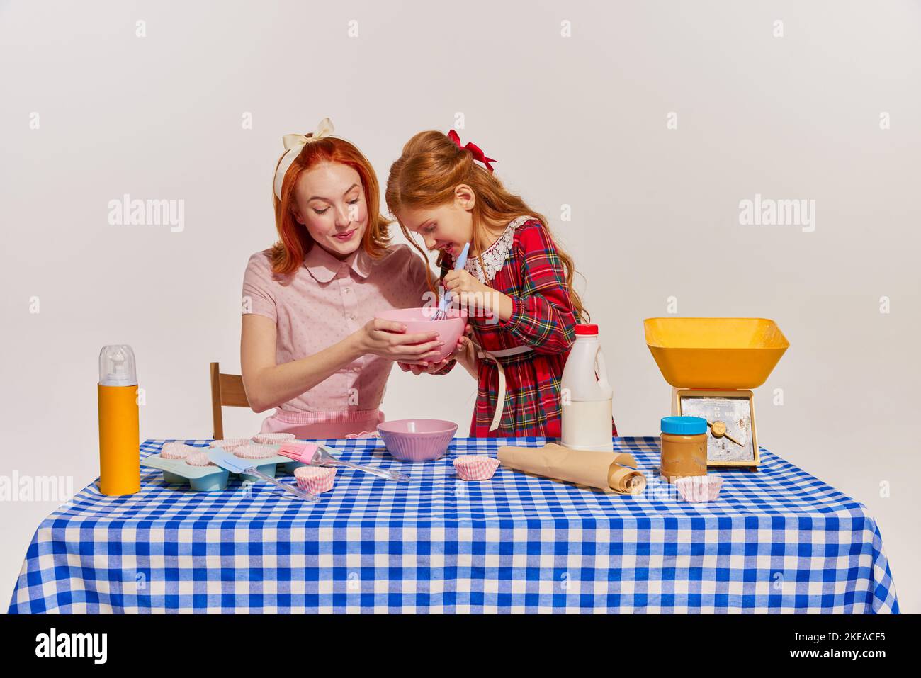 Portrait von Mutter und Tochter, die zusammen Kuchen kochen, isoliert auf grauem Hintergrund. Zeit zusammen verbringen Stockfoto