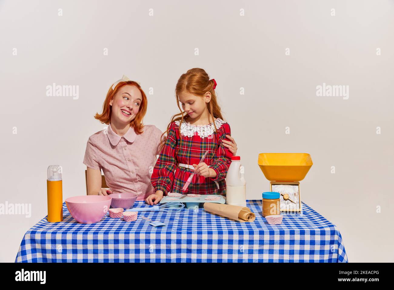 Portrait von Mutter und Tochter, die zusammen Kuchen kochen, isoliert auf grauem Hintergrund. Hobby für Mädchen Stockfoto