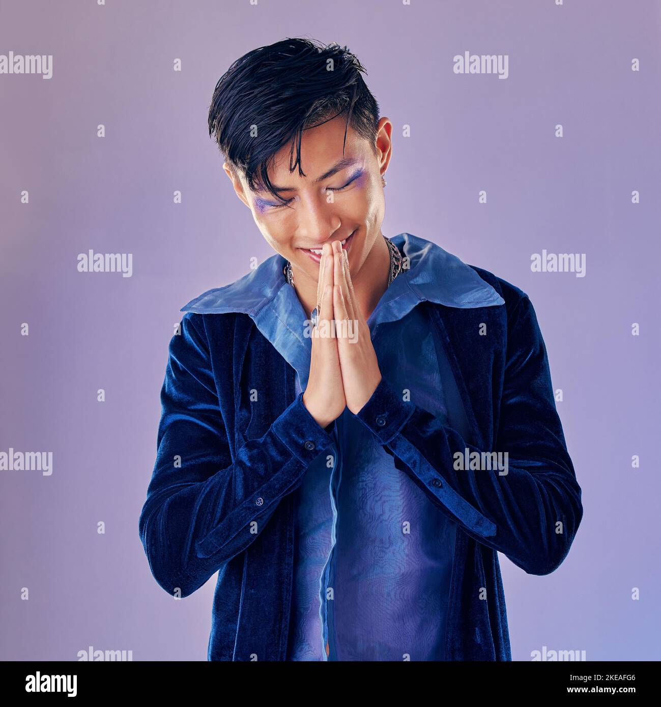 Mann, Mode Make-up oder Punk Rock Hände in danke, willkommen oder japanischen Gruß auf kreative lila Hintergrund Studio. Lächeln, glücklich oder künstlerisch Stockfoto