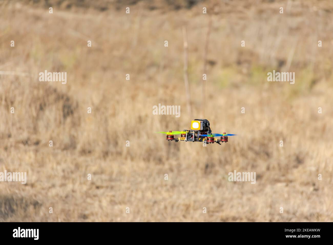 Fliegende Quadcopter-Drohne am Boden mit gelben Kräutern im Hintergrund verschwommen. Ansicht des nicht manierten Fahrzeugs auf Bodenebene. Stockfoto