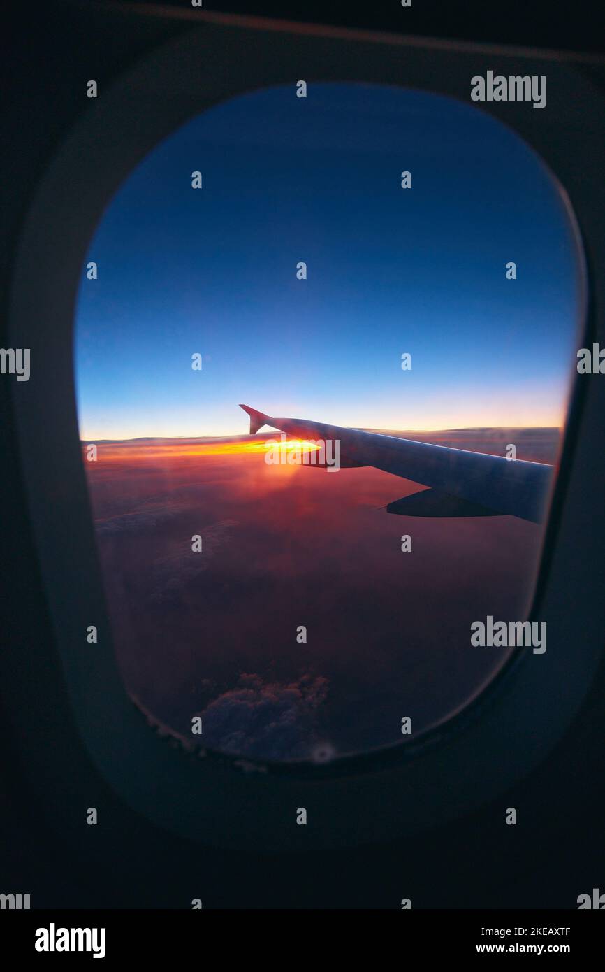 Wunderschöner Blick auf den Sonnenaufgang durch das Bullauge während des Fluges. Flugzeug Flügel über dem bewölkten bunten Sonnenuntergang Stockfoto