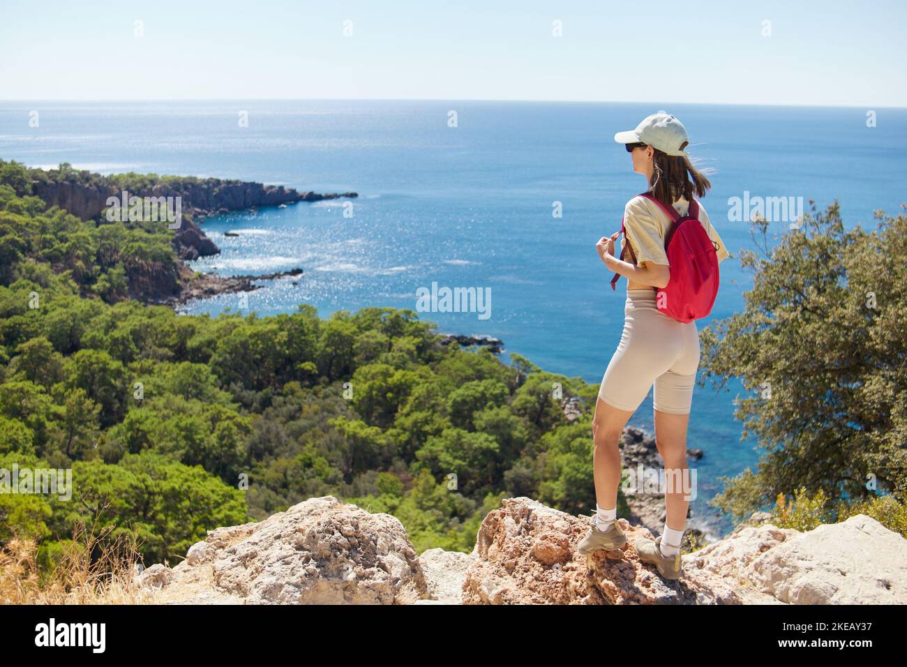 Die junge Frau mit pinkem Rucksack steht während der Wanderung gegen die natur der mittelmeerküste Stockfoto