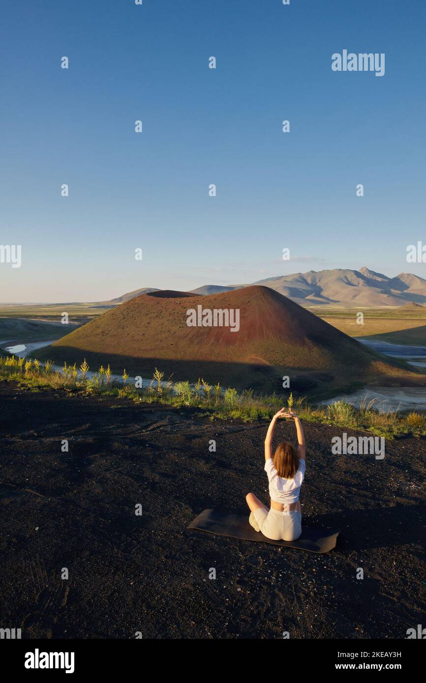 Eine junge Frau steht in einer Yoga-Pose vor der wunderschönen Naturlandschaft von Tal, vulkanischem See und Krater Stockfoto