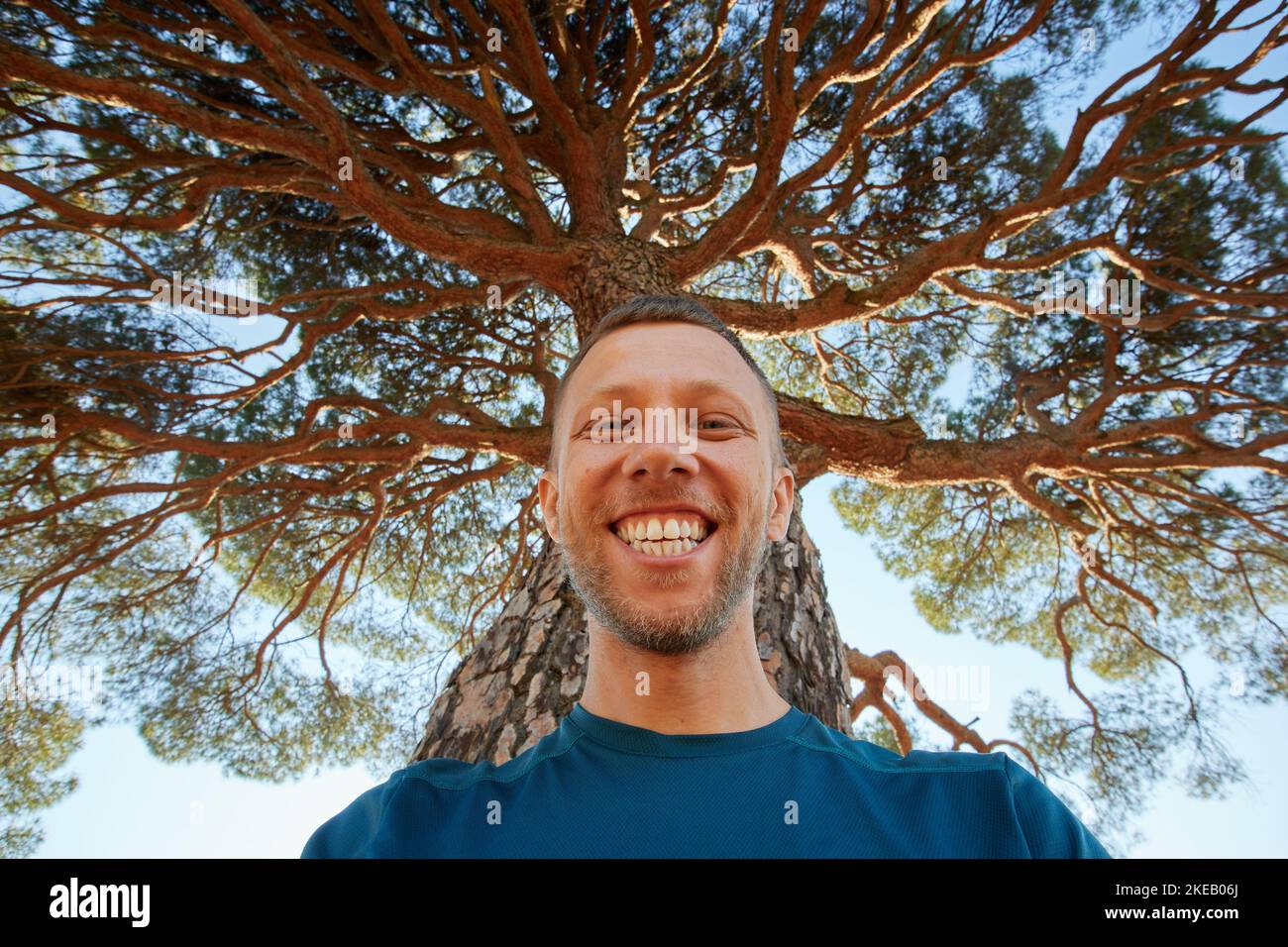Glücklich lachender Mann in der Natur unter dem großen Baum. Ein Mann mit einem Lächeln unter der Baumkrone Stockfoto