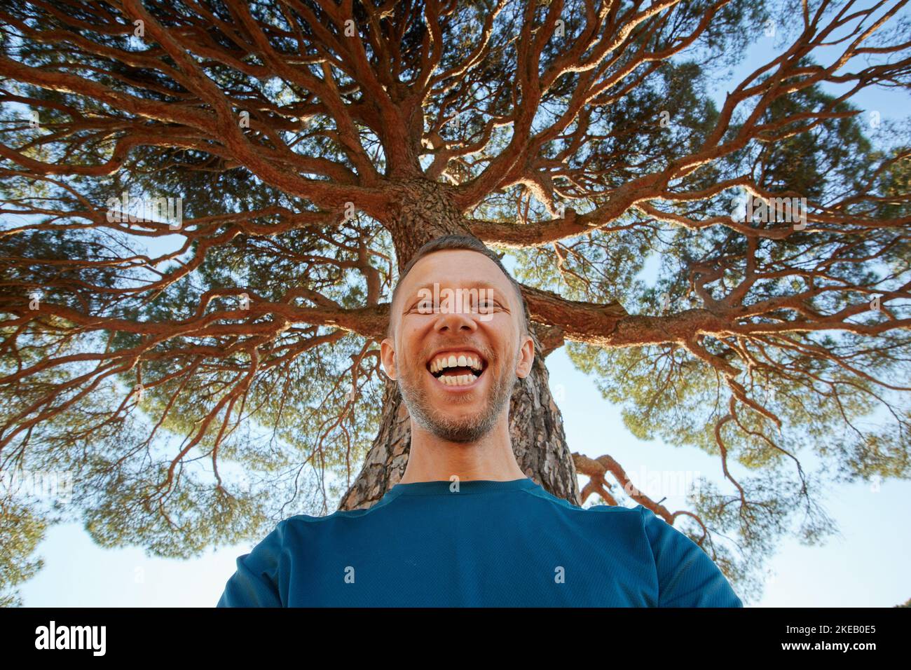 Glücklich lachender Mann in der Natur unter dem großen Baum. Ein Mann mit einem Lächeln unter der Baumkrone Stockfoto