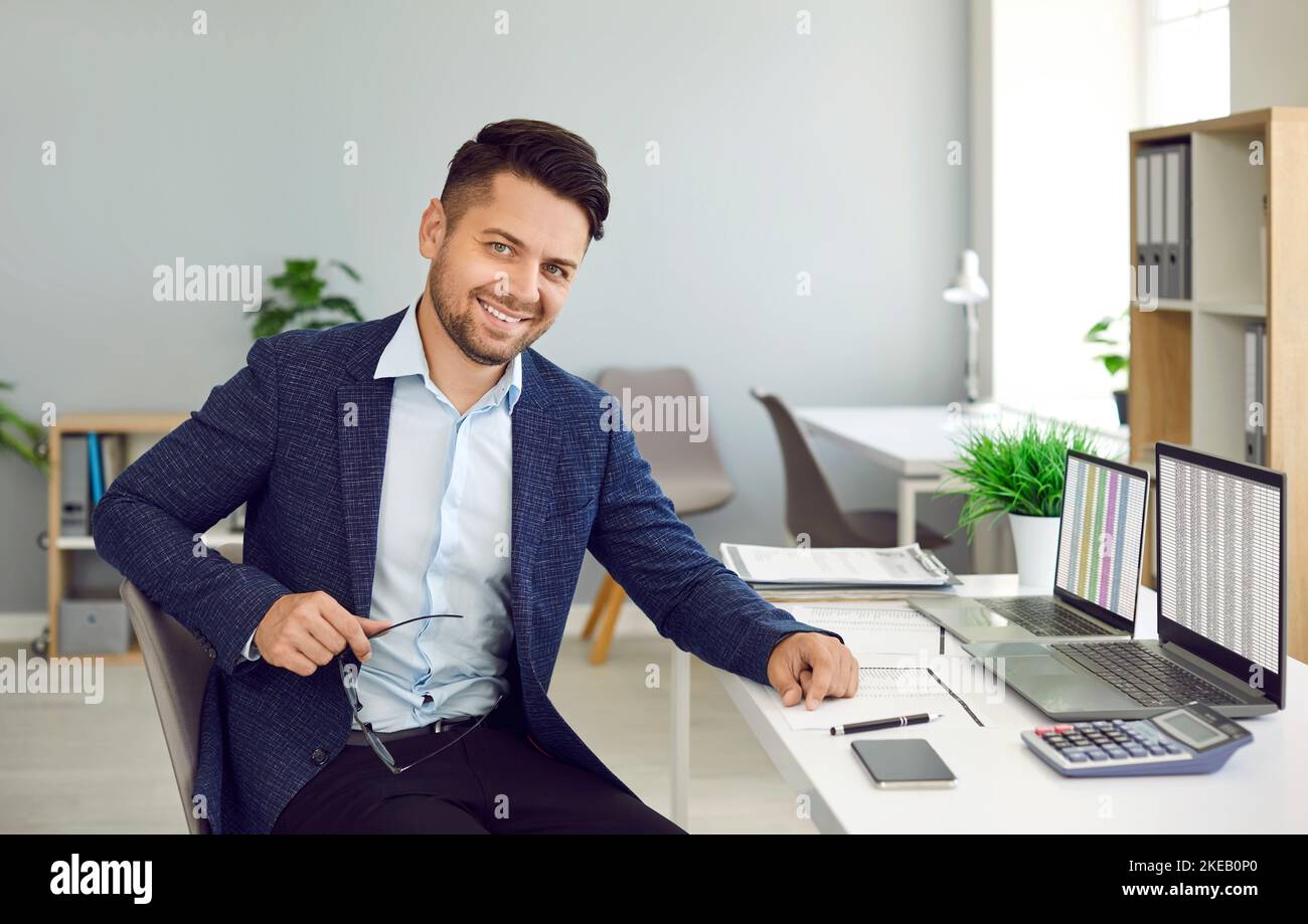 Porträt eines glücklichen männlichen Geschäftsbuchhalters, der mit einem Laptop am Schreibtisch sitzt Stockfoto