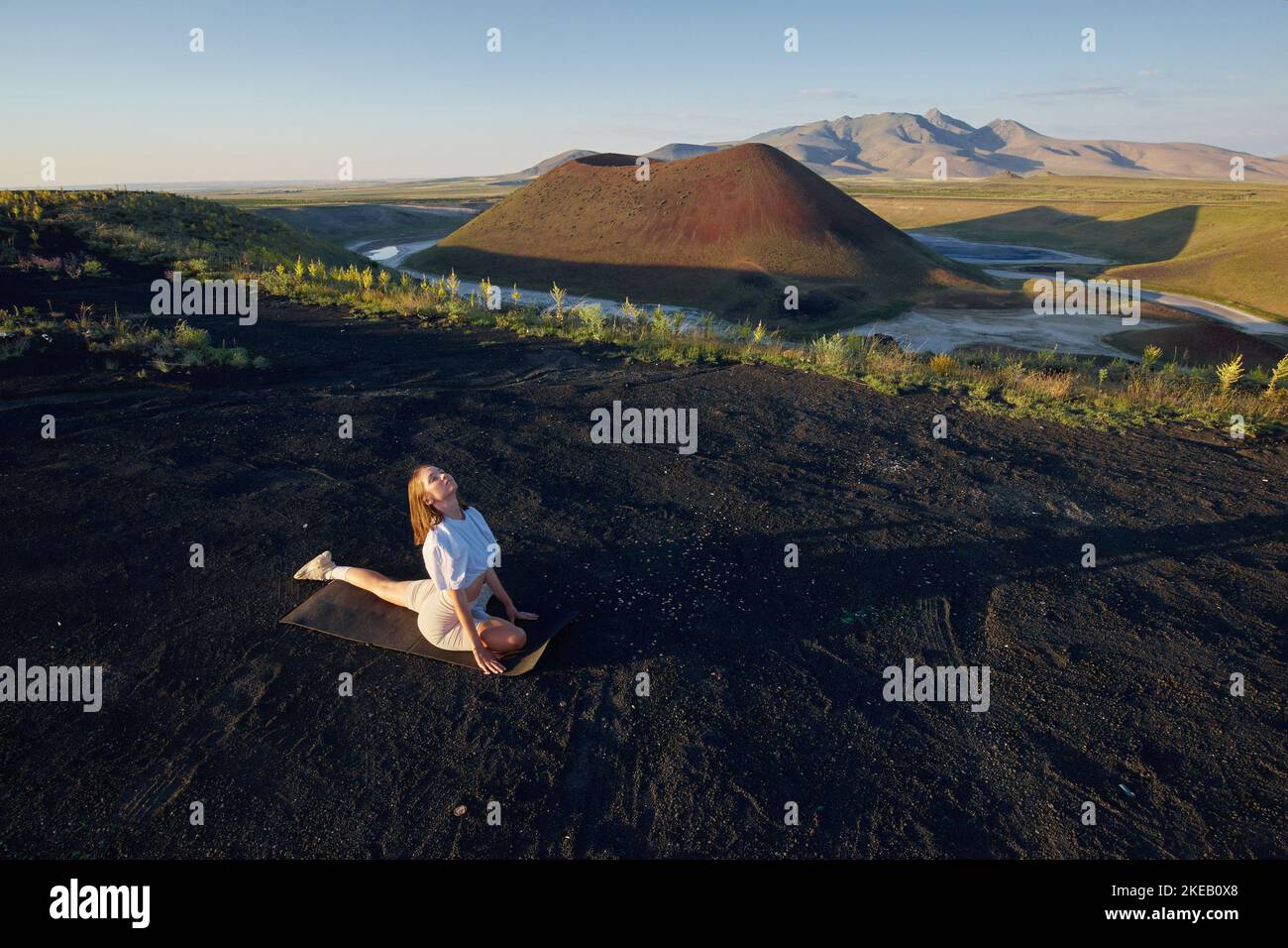 Eine junge Frau steht in einer Yoga-Pose vor der wunderschönen Naturlandschaft von Tal, vulkanischem See und Krater Stockfoto