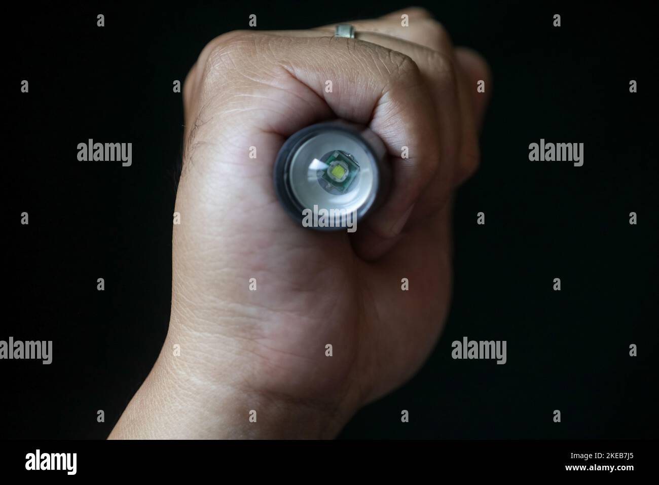 Eine LED-Taschenlampe, die in der Hand einer Person auf einem schwarzen Hintergrund gehalten wird. Nahaufnahme. Stockfoto