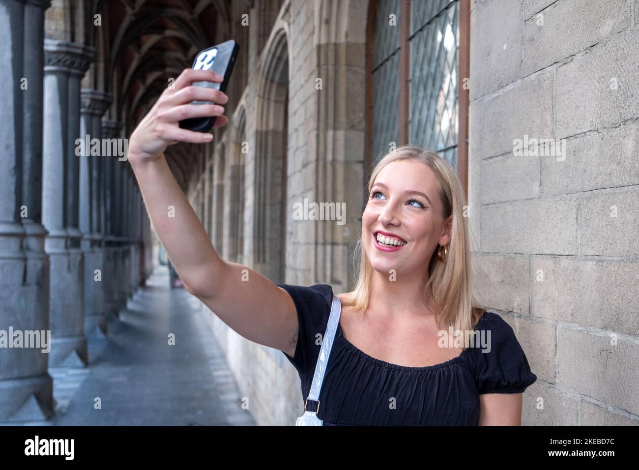 Porträt von wunderbaren weißen weiblichen Modell mit hellen Make-up, die Energie in guten Tag in Europa. Schöne blonde Frau in stilvoller Kleidung macht Selfie, während sie an einem alten Gebäude vorbeigeht. Hochwertige Fotos Stockfoto