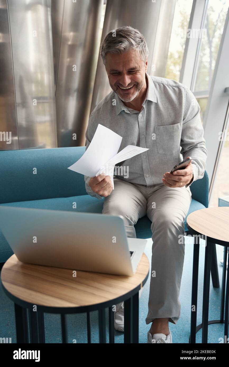 Ein fröhlicher Mann mittleren Alters sitzt auf dem Sofa in einem Erholungsgebiet Stockfoto