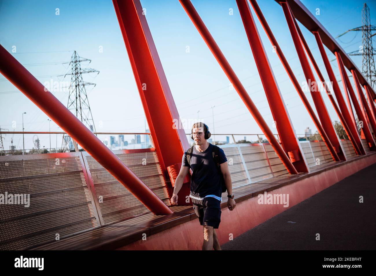 Ein junger Mann mit Kopfhörern, der ein T-Shirt und Shorts trägt und auf einer Brücke läuft Stockfoto