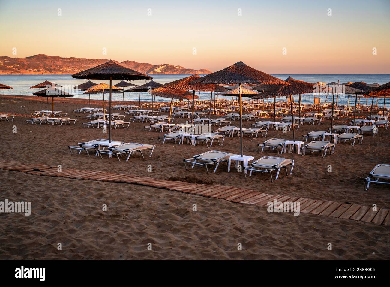 Leerer Strand mit Sonnenschirm und Liegestuhl in schöner Sonnenaufgangsbeleuchtung. Amoudara, Kreta, Strand. Stockfoto