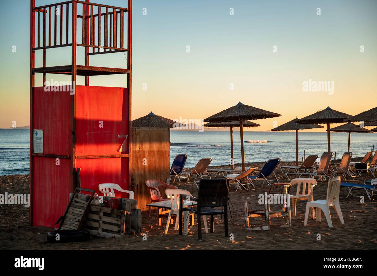 Roter Rettungsschwimmer Turm, Sonnenschirm und Stuhl am leeren Strand in idyllischer Sonnenaufgangsbeleuchtung. Amoudara, Kreta, Greec. Stockfoto