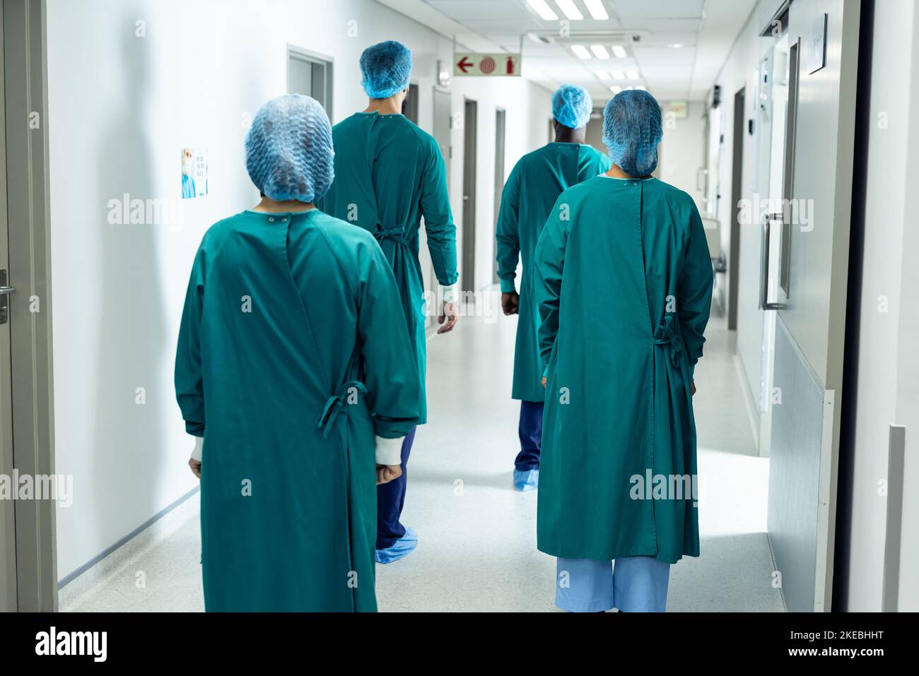 Rückansicht von vier Chirurgen in Operationskappen und Kitteln im Krankenhausgang Stockfoto