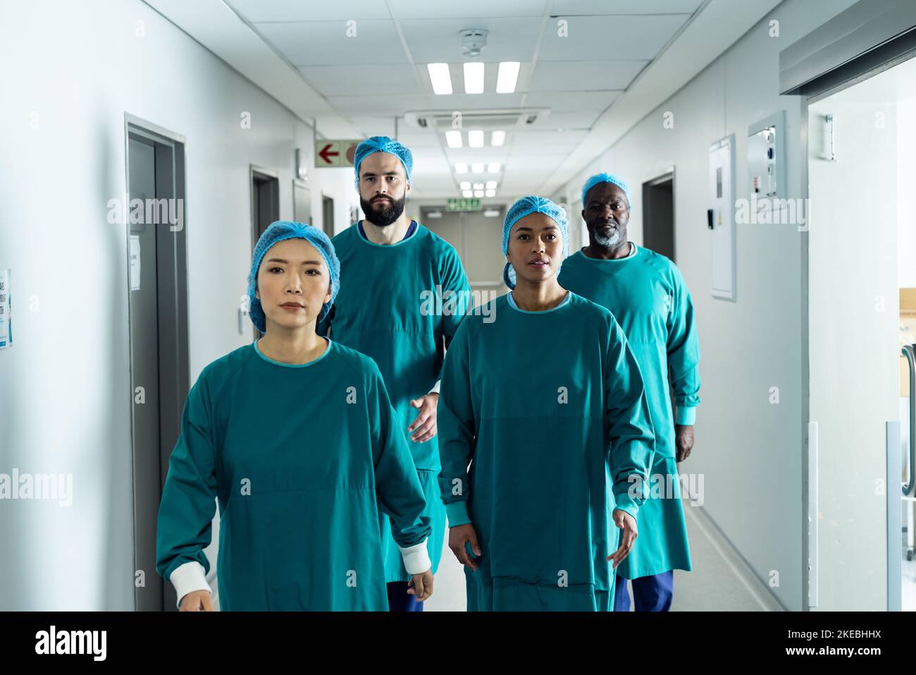 Vielfältige Gruppe von vier Chirurgen in Operationskappen und Kitteln im Krankenhausgang Stockfoto
