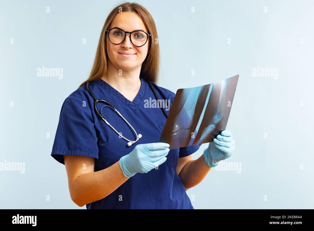 Ärztin untersucht Röntgenbild, bei dem eine Verletzung auf blauem Hintergrund diagnostiziert wird Stockfoto