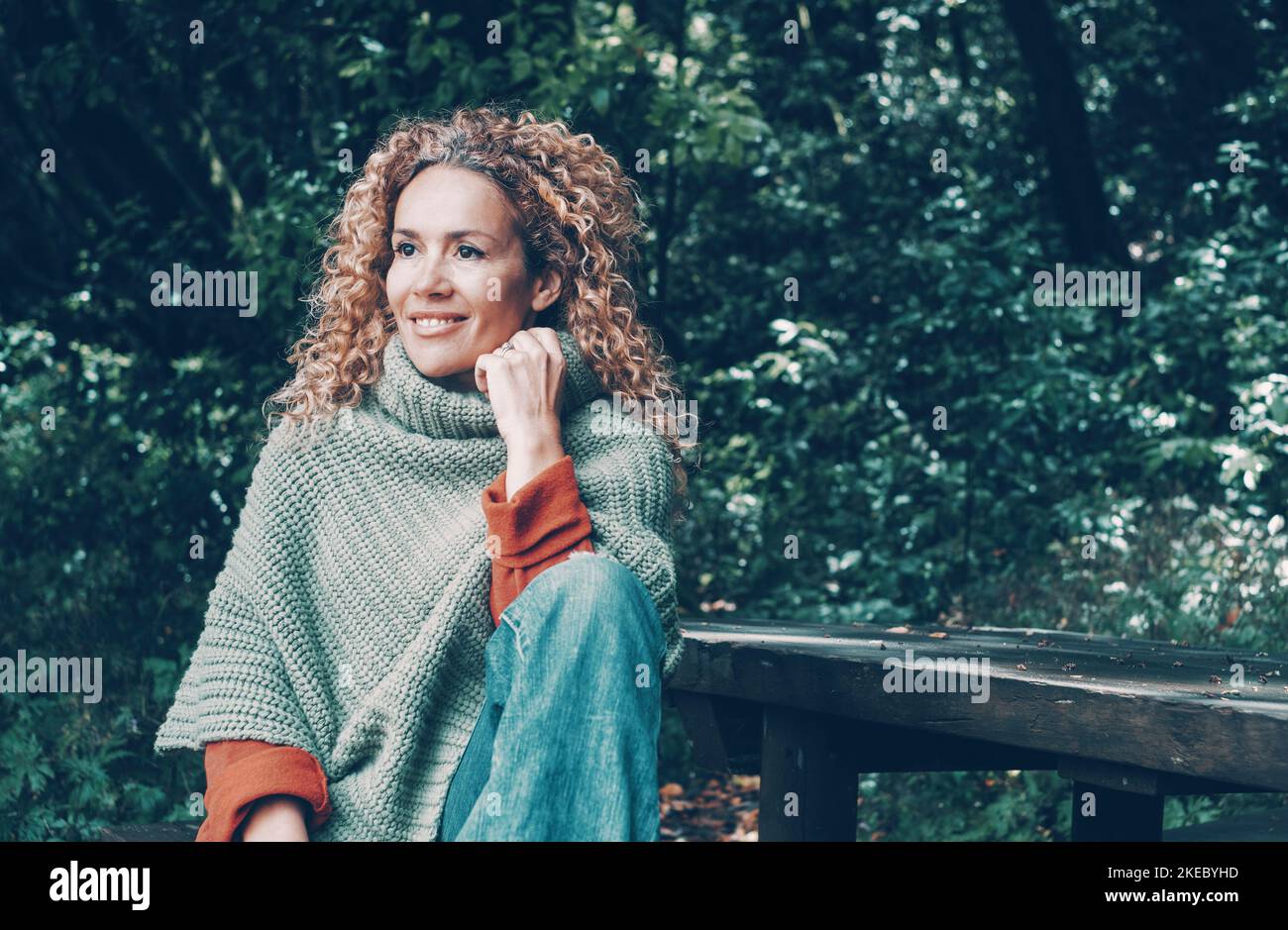 Portrait einer fröhlichen jungen reifen Frau, die lächelt und die Freizeit im Freien genießt, die im Park mit grünen Bäumen und schöner Natur im Hintergrund sitzt. Touristen Menschen unabhängiges Frauenleben Stockfoto