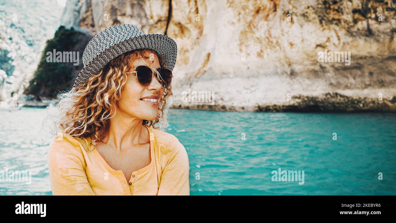 Outdoor-Porträt von attraktiven touristischen Frau smiellig und genießen Outdoor-Freizeitaktivitäten mit einem blauen See oder Fluss im Hintergrund. Glückliche weibliche Menschen mit har und Sonnenbrille und trendigen Stil Stockfoto