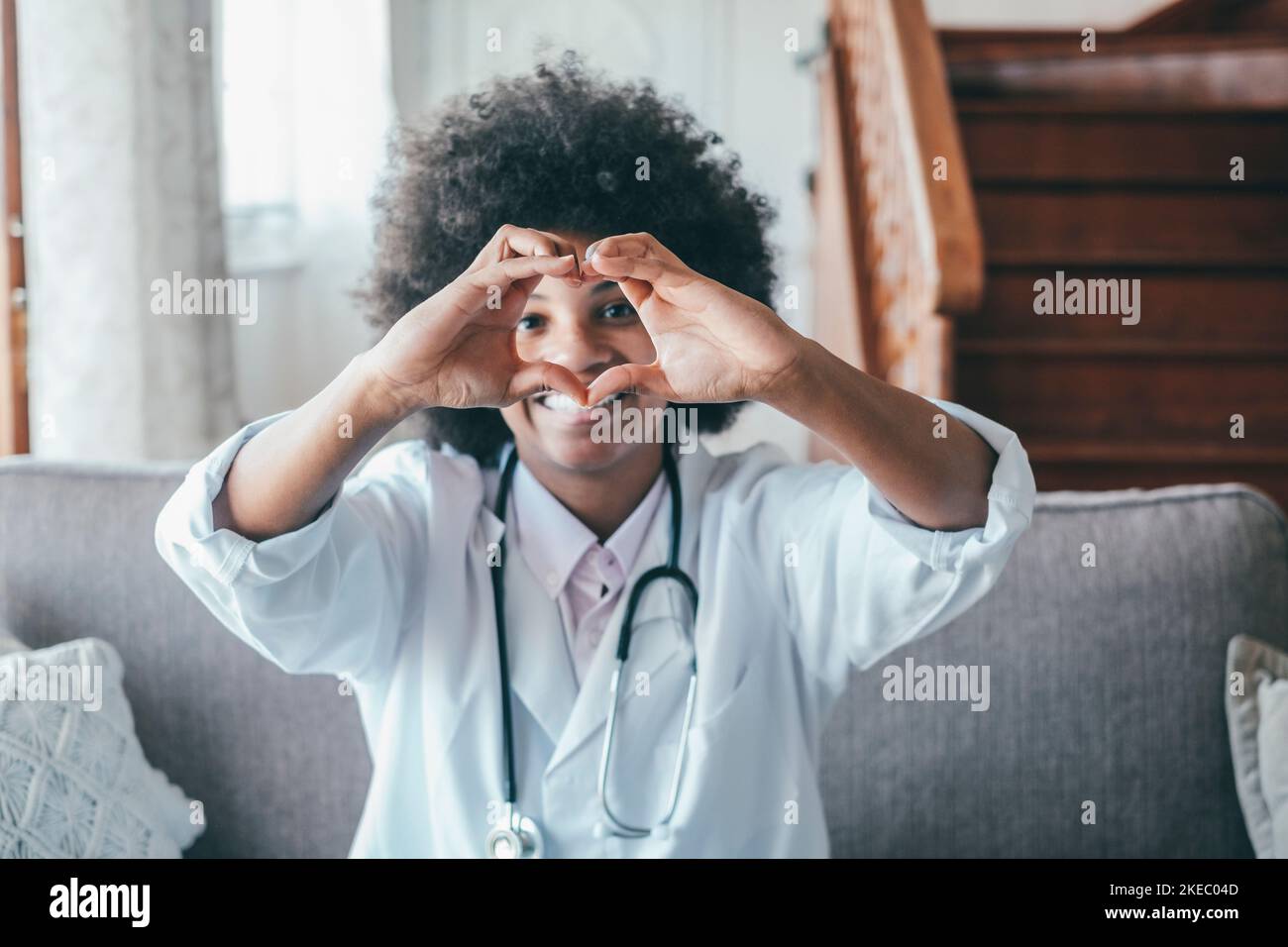 Ärztin macht eine Geste der Herzform mit den Händen. Lächelnde schwarze Ärztin, die mit ihren Händen ein Liebessymbol macht. Mitarbeiter im Gesundheitswesen, der den Patienten Liebe und Unterstützung gibt Stockfoto