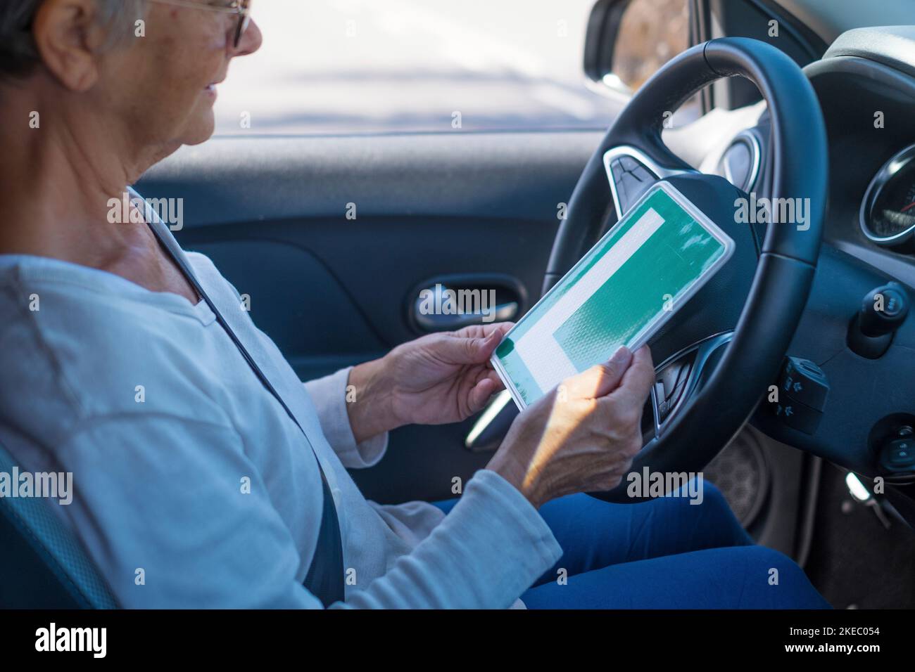 Eine alte Frau, die im reifen Alter einen Pass für ein Auto bekommt. Senior schaut auf die L-Genehmigung im Fahrersitz Stockfoto