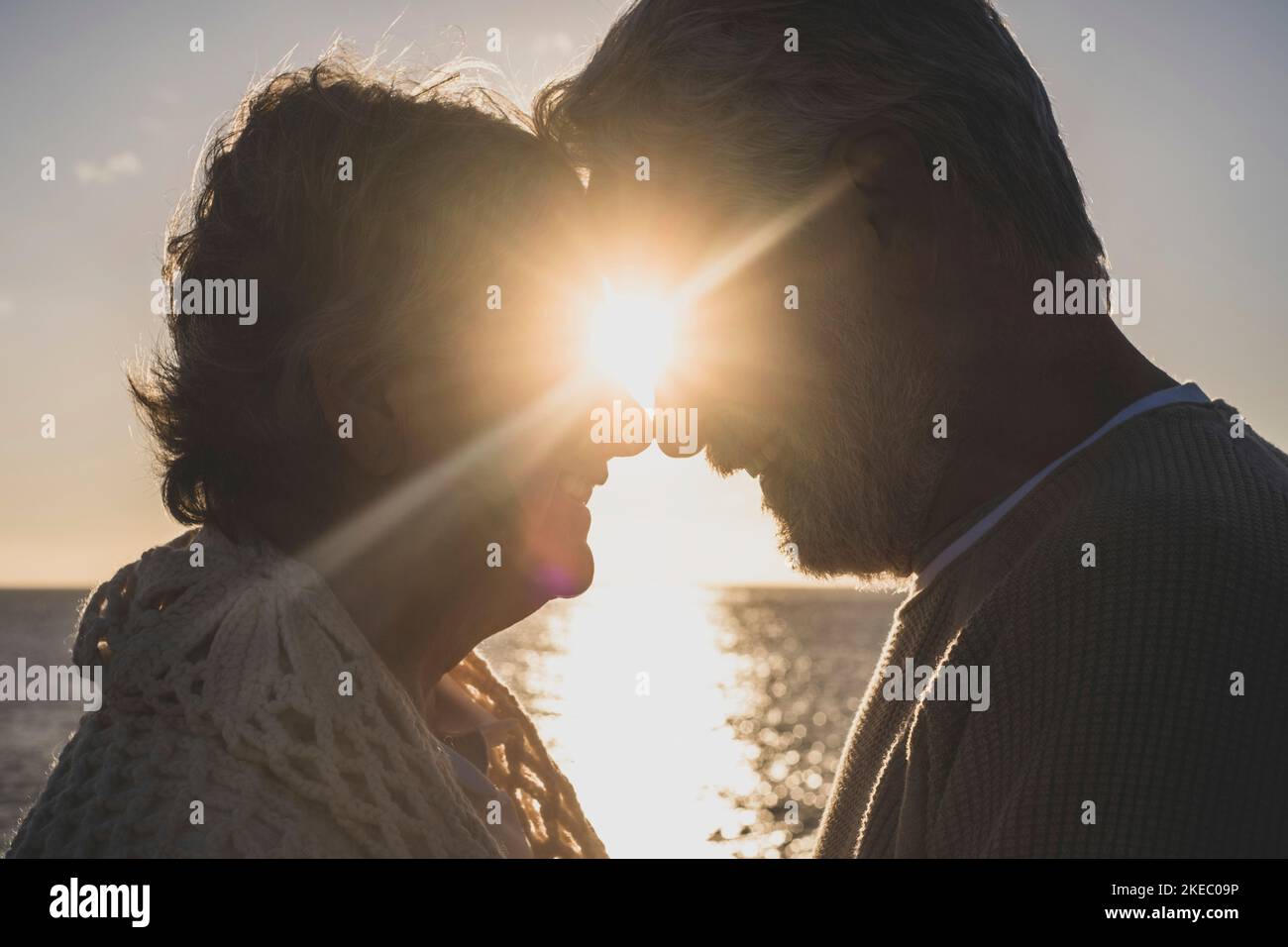 Porträt und Nahaufnahme von zwei verliebten Senioren, die sich gegenseitig zuschauen und die Sonne des Sonnenuntergangs zwischen ihren Köpfen lächeln Stockfoto