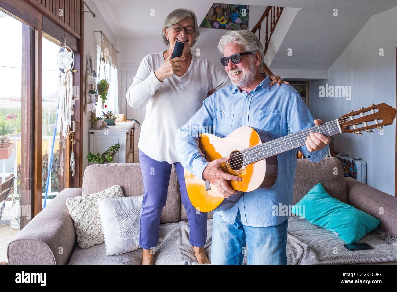 Fröhliche und lustige Paare alter und reifer Menschen, die Spaß haben und zu Hause eine gemeinsame Party machen, singen und tanzen, um die Gitarre drinnen zu spielen. Urlaub oder sogar feiern Konzept. Stockfoto